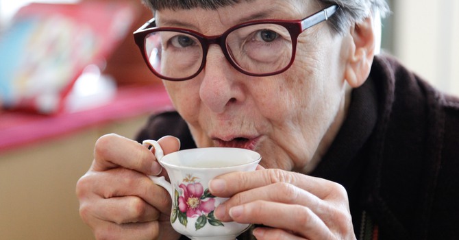 Äldre kvinna med glasögon håller en blommig porslinskopp till sin mun.