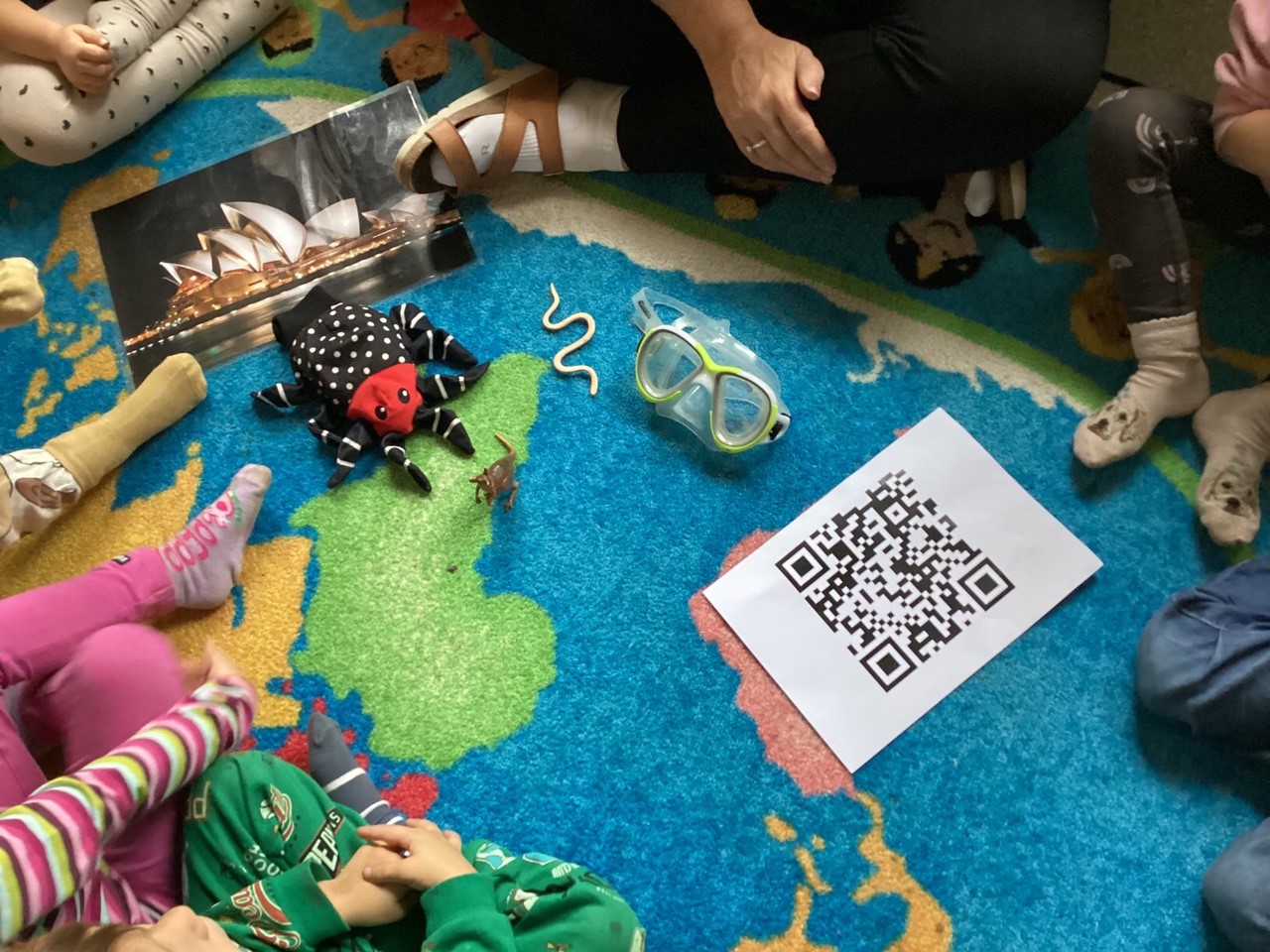Barn som sitter på golvet kring en karta över Australien med en QR-kod.