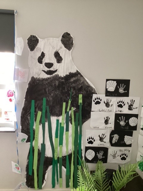 Panda i helfigur i papper samt barnens handavtryck uppsatta på en vägg.