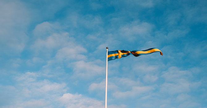 Svenska flaggan som vimpel i vinden mot blå himmel och skira moln.