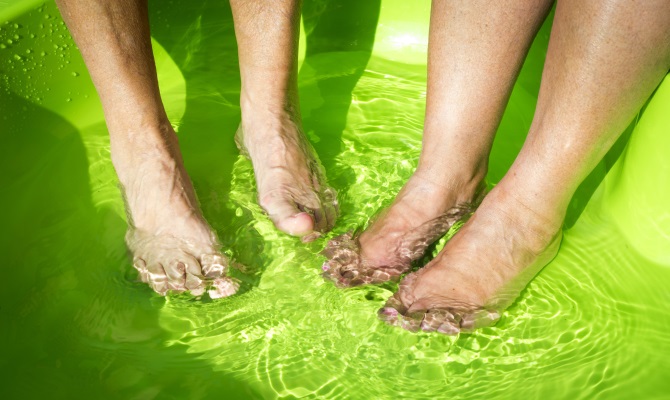 två personer som tar ett gemensamt fotbad i en grön balja.