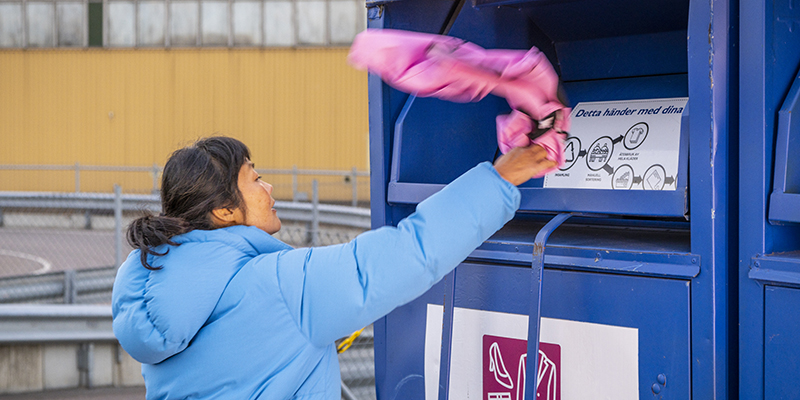 Kvinna slänger ett klädesplagg i en insamlingsbox för textilier.