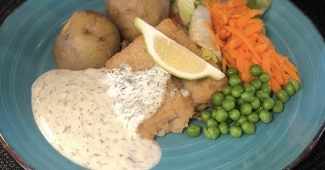 Pannerad fisk, potatis och kall dillsås på en blå tallrik.