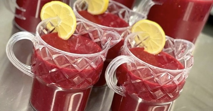 Röd fruktkräm i plastbringare med en citronskiva på kanten.